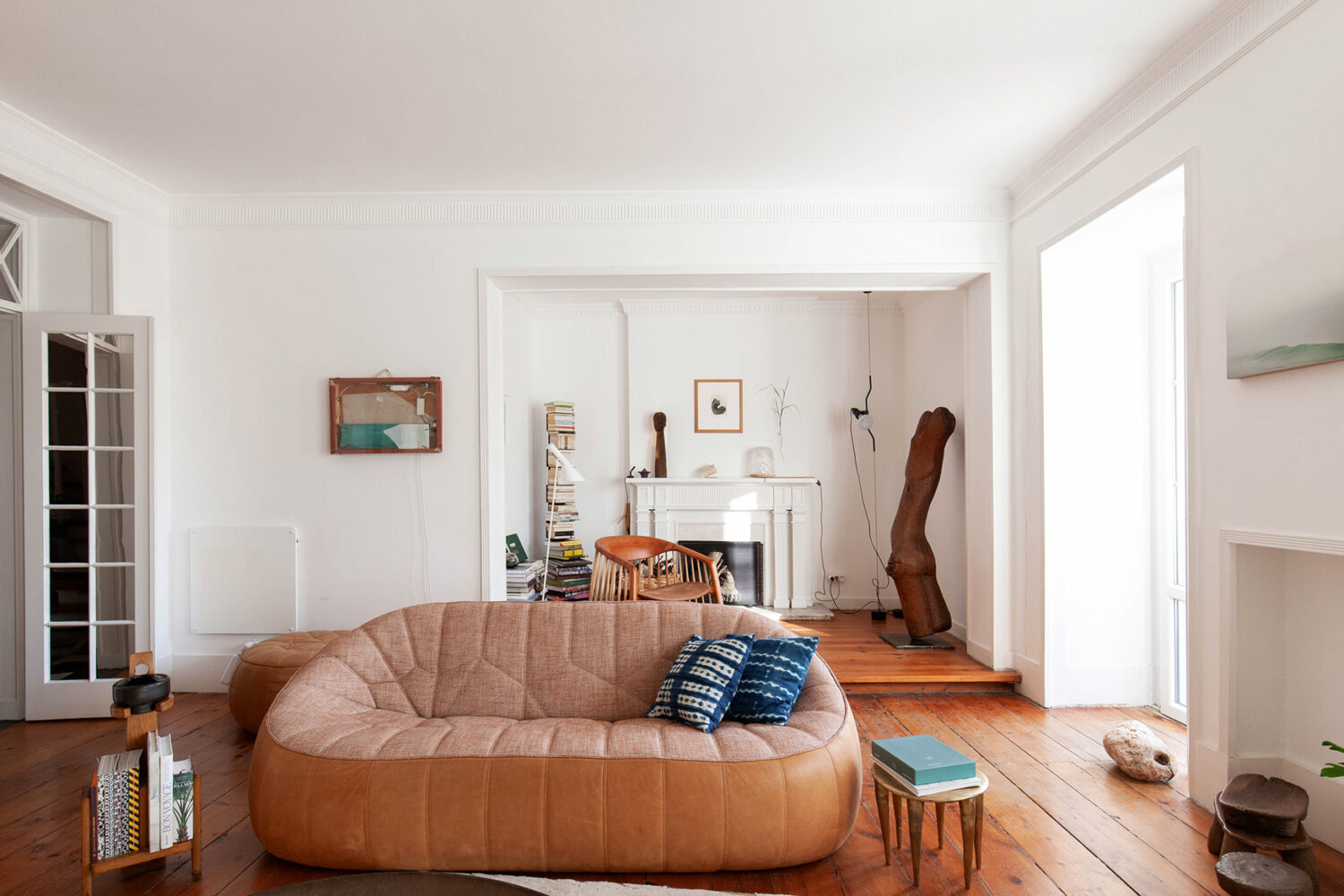 Warme Holz- und Ledertöne dominieren das Wohnzimmer mit Ottoman Sofa, Beistelltisch Zindi aus Bronze von Charlotte Thon und Marc Boinet und Skulptur von Bertrand Bougé.